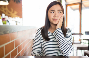 Young woman at restaurant, holding jaw and wondering what to eat